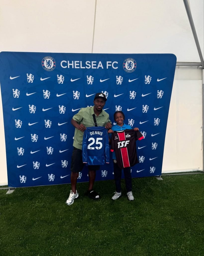 Coach Mali holding a Chelsea FC shirt beside a young TSF player at a Chelsea FC event