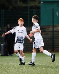 Two young TSF players in white kits celebrating together during a match