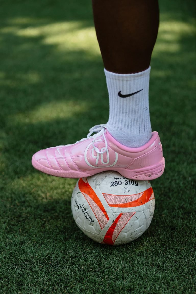 Pink boot resting on a football on the grass