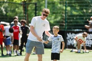 A TSF coach handing a trophy over to a young player in a white and gold kit