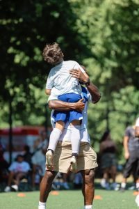 A coach lifting a young player into the air to celebrate winning his 1v1 round