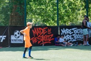 A young player in orange walking past the Made In The Streetz and More Touches More Tekkers banners