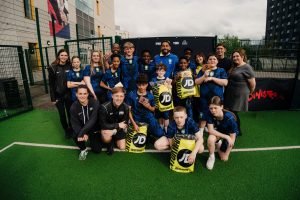 The full squad of young players and coaches posing together on the pitch holding their JD Sports bags and gift cards
